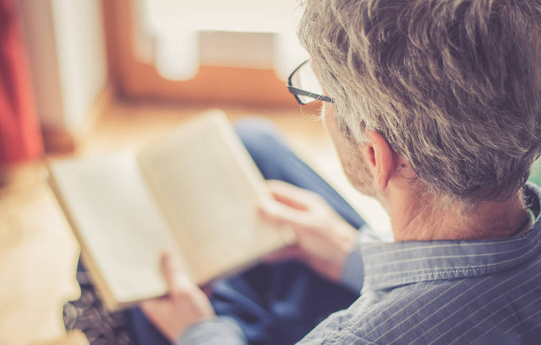 Senior man is reading a book at home, selective focus - Foto, afbeelding
