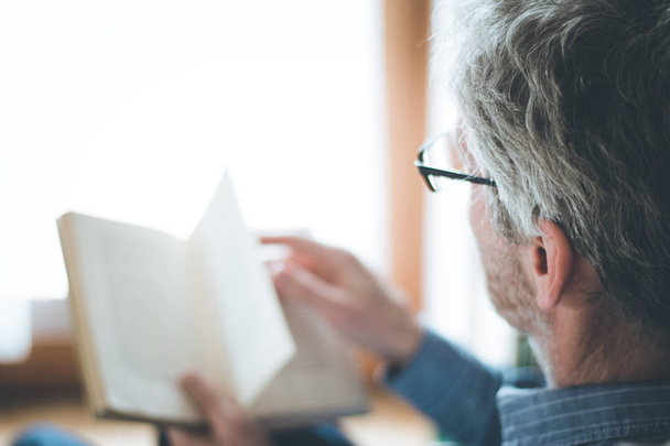 Senior man is reading a book at home, selective focus - Fotoğraf, Görsel