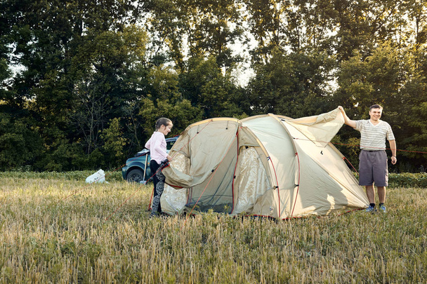 Family set up tent camp at sunset, beautiful summer landscape. Tourism, hiking and traveling in nature. - Foto, immagini