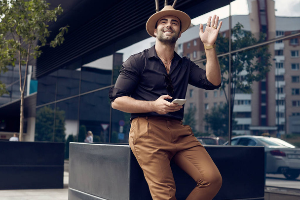 schöner braungebrannter muskulöser Hipster in schwarzem Hemd und Hut mit Handy - Foto, Bild