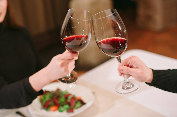 Мужчина и женщина пьют красное вино. На картинке крупным планом руки в очках - Фото, изображение