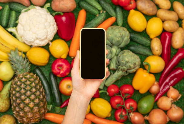 Crop hand with blank smartphone over fruits and vegetables - Photo, Image