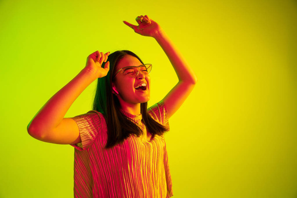 Beautiful girls facial expression in neon light on yellow studio background - Photo, image