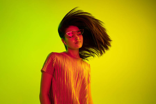 Beautiful girls facial expression in neon light on yellow studio background - Photo, Image