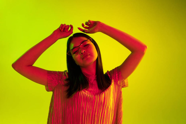 Beautiful girls facial expression in neon light on yellow studio background - Foto, Imagem