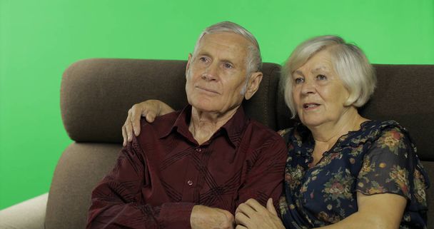 Üst düzey yaşlı adam ve kadın bir kanepede birlikte oturan ve TV izliyor. Chroma anahtarı - Fotoğraf, Görsel
