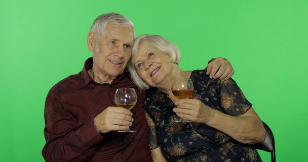 Senior aged man drinking white wine with a elderly woman companion on chroma key - Photo, Image