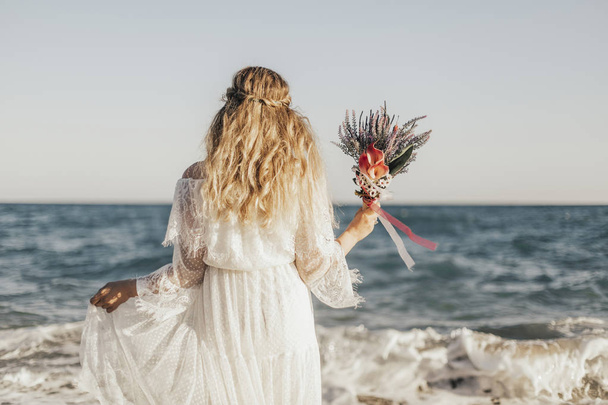 The bride standing by the sea and the flowers in her hand - Foto, imagen