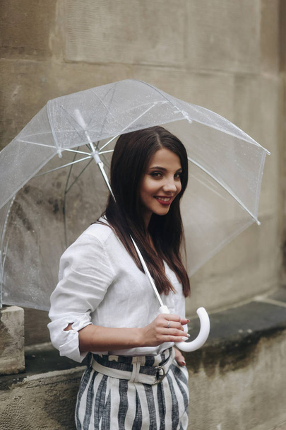 Vertical portrait of a happy girl with umbrella near old house. Copy space. It's summer rain. - Foto, imagen