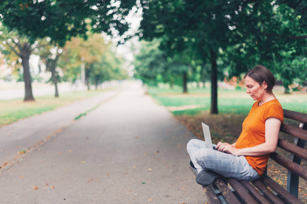 Woman using laptop computer on park bench - Photo, Image