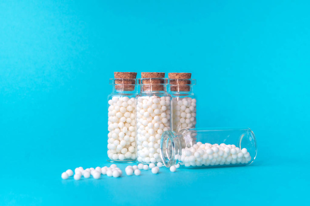 Homeopaattisia palloja neljässä lasipullossa sinisellä pohjalla. Pallot ovat hajallaan yhdestä pullosta. Vaihtoehtoinen homeopatia lääke yrttejä, terveydenhuollon ja pillereitä käsite. Kopioi tilaa tekstille
 - Valokuva, kuva