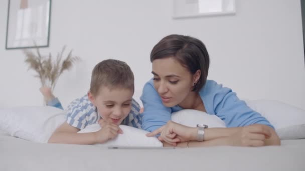 Happy young mother showing cartoon on digital tablet to her toddler son before going to sleep. Happy mother showing cartoon on digital tablet to her toddler son. - Video