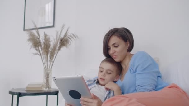Anne ve oğlu evde yatak odasında dijital tablet kullanarak. Evde yatak odasında dijital tablet kullanarak mutlu Kafkas anne ve oğlu ön görünümü. - Video, Çekim