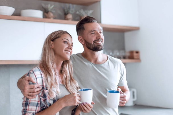 young couple drinking coffee standing in the kitchen - Foto, afbeelding