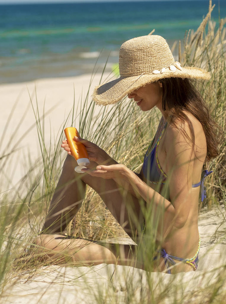 Mooie vrouw weet hoe de veiligheid van de zon. Ze draagt een hoed en past een zonnebrandcrème toe. - Foto, afbeelding