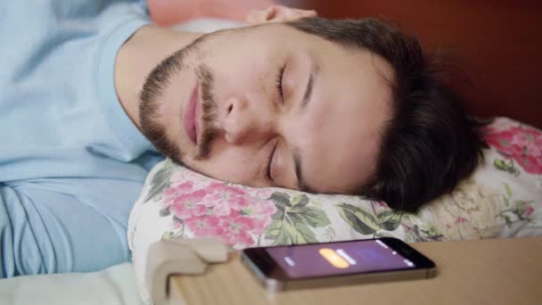 Homem com cabelo escuro deita na cama com travesseiro confortável, acorda e olha para o telefone
 - Filmagem, Vídeo