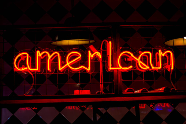 Glowing Neon red sign AMERICAN and blurred lights on black background. - Photo, Image