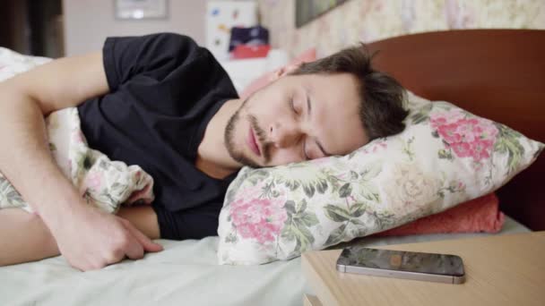 Man with dark hair lays on bed with comfy pillow and cell put on bedside table - Metraje, vídeo