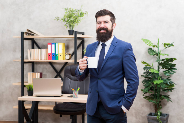 Man bearded businessman hold coffee cup stand office background. Drinking coffee relaxing break. Boss enjoying energy drink. Start day with coffee. Successful people drink coffee. Caffeine addicted - Foto, Imagen