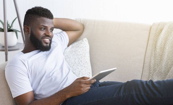 デジタルタブレットでインターネットを閲覧する陽気なアフリカ系アメリカ人の男 - 写真・画像