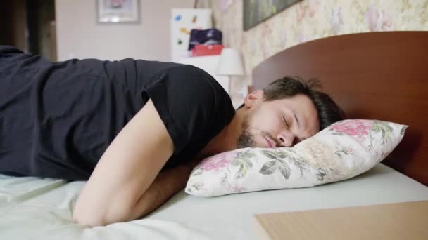 Ο άνθρωπος με τα σκούρα μαλλιά κοιμάται στο κρεβάτι με το μαξιλάρι, κυλά πάνω και ξυπνάει αργά. - Πλάνα, βίντεο