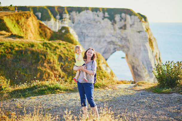 Happy young woman holding adorable toddler girl near famouse cliffs in Etretat - 写真・画像