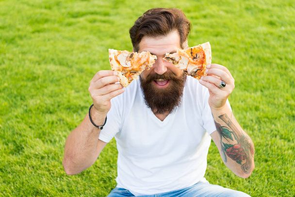 Delicious slice. Man bearded hipster eating delicious pizza. Cheerful guy eat pizza. Summer picnic concept. Caucasian male loving Italian traditional food. Hungry greedy man hold pizza in both hands - Valokuva, kuva