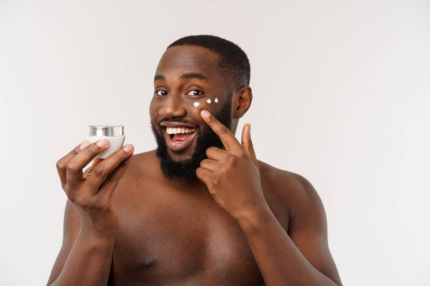 Glimlachend Afro man die crème op zijn gezicht aanbrengt. Mans Skin Care concept - Foto, afbeelding