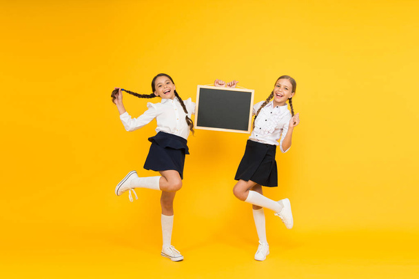 Back to school. Happy children holding school blackboard on yellow background. Little girls preparing for school lesson. Small kids smiling in school uniform on september 1, copy space - Photo, Image