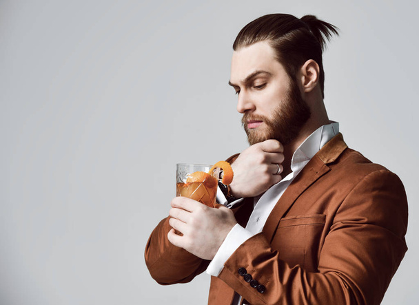 Young modern man bearded clubber in fashion suit looks thoughtfully into the glass with fresh cocktail mohito - Φωτογραφία, εικόνα