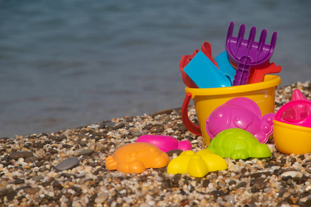 Kleurrijk plastic speelgoed voor kinderen liggend op kiezelstrand op zee achtergrond  - Foto, afbeelding