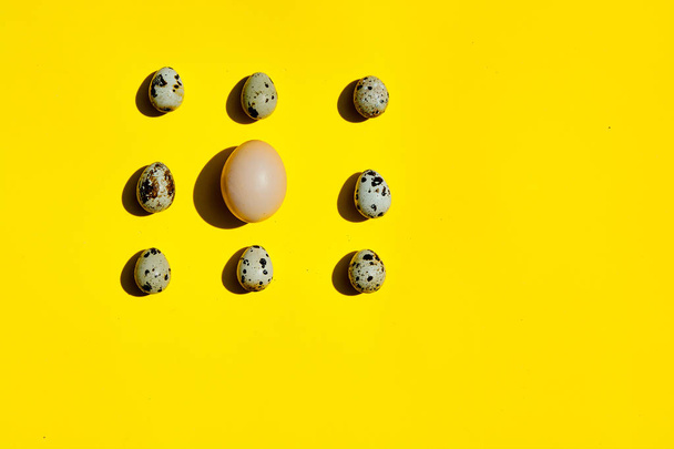 Σετ από μεγάλο αυγό κοτόπουλου και μικρά αυγά ορτυκιού στη σειρά σε κίτρινο φόντο. - Φωτογραφία, εικόνα