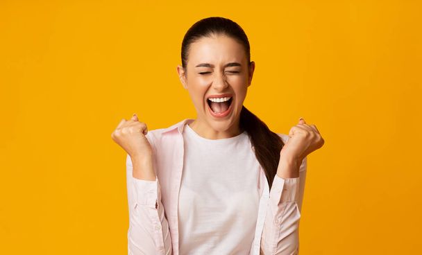 Woman Shouting Loudly And Shaking Clenched Fists On Yellow Background - Photo, Image