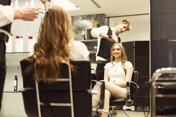 Парикмахер создает кудрявую прическу для улыбающейся девушки в салоне
 - Фото, изображение
