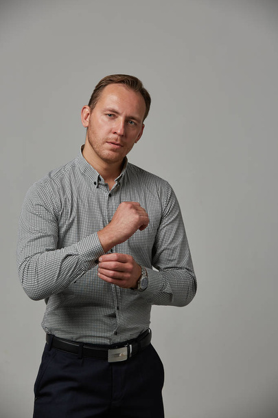 A young man in a gray shirt looks at the clock on his hand. Emotional, brave face. Isolated on white background Copy space Advertising and commercial design. - Valokuva, kuva