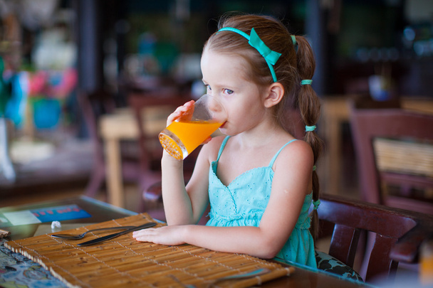 Adorable petite fille qui prend le petit déjeuner et boit du jus au restaurant de la station
 - Photo, image