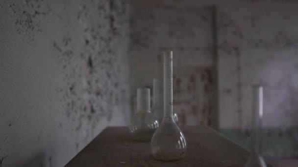 Okrągłe kolby medyczne i brudne rurki są na shabby stole w starej sali w SLO-mo - Materiał filmowy, wideo