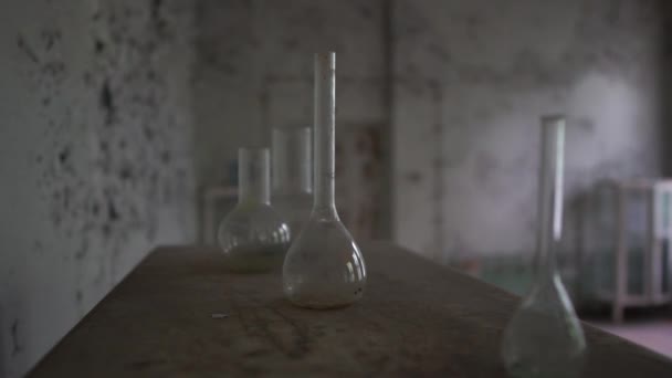 Ronde chemische kolven en groezelige buizen zijn op een vuile tafel in de oude hal in slo-mo - Video