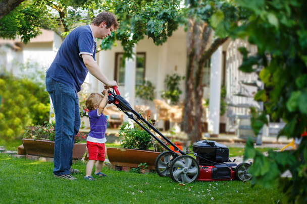 Mann und sein kleiner Sohn amüsieren sich mit Rasenmäher im Garten - Foto, Bild