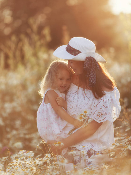 Gelukkige familie moeder met schattige kleine kind meisje in de Kamille veld in de zomer - Foto, afbeelding