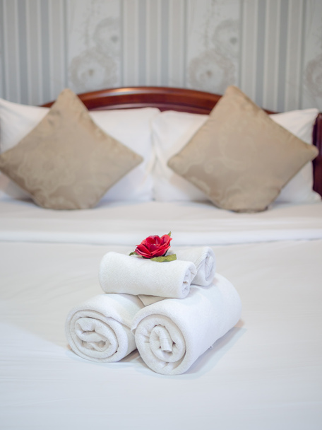 Λευκές καθαρές πετσέτες διακόσμηση με κόκκινο λουλούδι σε λευκό καθαρό κρεβάτι - Φωτογραφία, εικόνα
