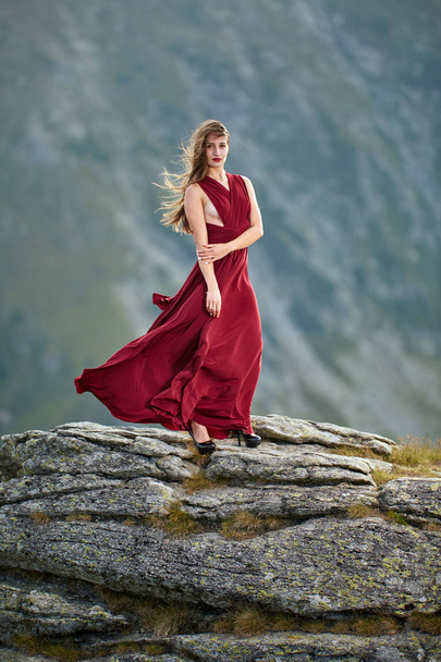 Mooie vrouwelijke mode model in rode jurk op berg rotsen - Foto, afbeelding