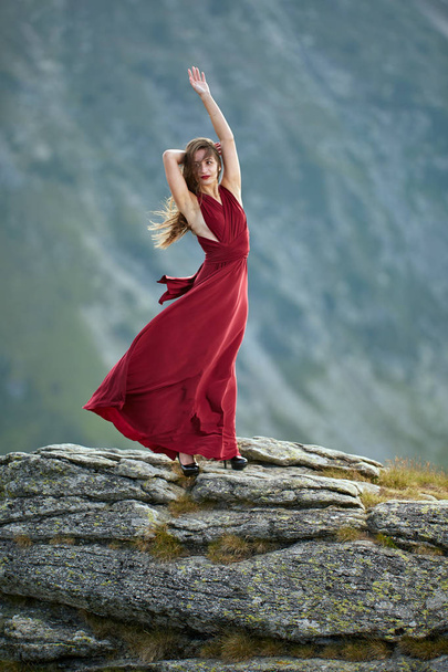 Όμορφο θηλυκό μοντέλο μόδας σε κόκκινο φόρεμα σε βράχους βουνό - Φωτογραφία, εικόνα