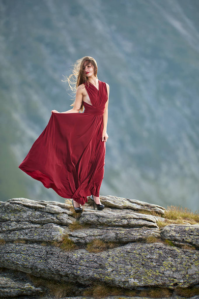 Krásný ženský módní model v červených šatech na horských skalách - Fotografie, Obrázek