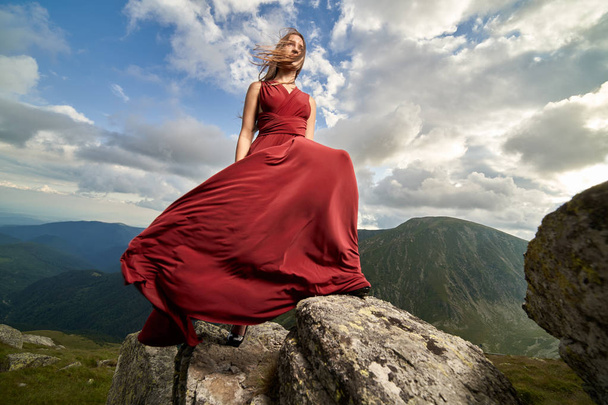 Bella modella femminile in abito rosso su rocce di montagna
 - Foto, immagini