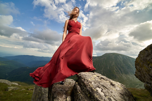 Όμορφο θηλυκό μοντέλο μόδας σε κόκκινο φόρεμα σε βράχους βουνό - Φωτογραφία, εικόνα