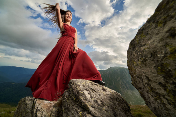 Beautiful female fashion model in red dress on mountain rocks - Фото, изображение