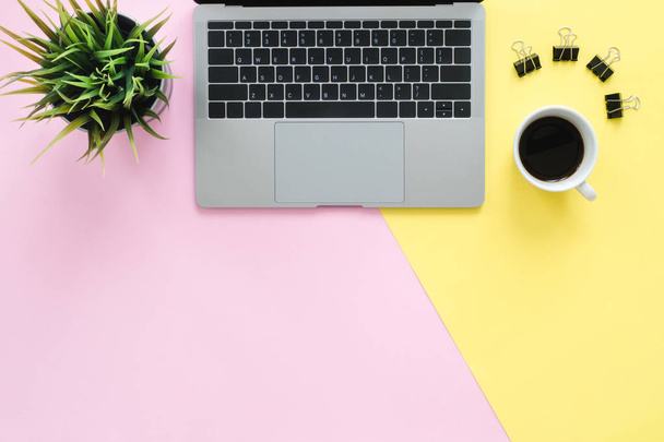 Irodai íróasztal működő hely - lapos feküdt felülnézet másol hely egy működő helyet a laptop, egy csésze kávét, és kis fű pasztell háttér forgalomba hozatalát. Pasztell sárga rózsaszín háttér tér fogalma. - Fotó, kép