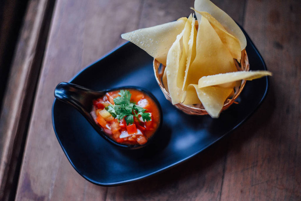 Tomato salsa and corn chips on wood table , Fresh tomato salsa with serrano pepper, red onion, green onion, lime, and cilantro in black dish - Foto, Imagem