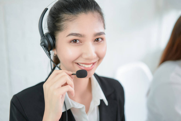 Lächelnde asiatische Unternehmensberaterin mit Mikrofon-Headset des Kundendiensttelefonisten am Arbeitsplatz. - Foto, Bild